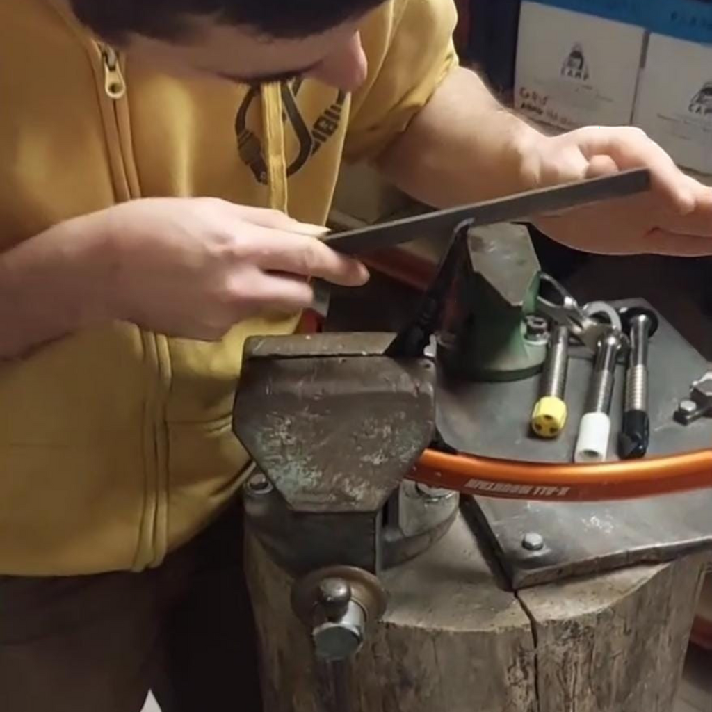 Technicien 4c+ affûtant manuellement la lame d'un piolet fixé dans un étau pour une précision optimale en escalade