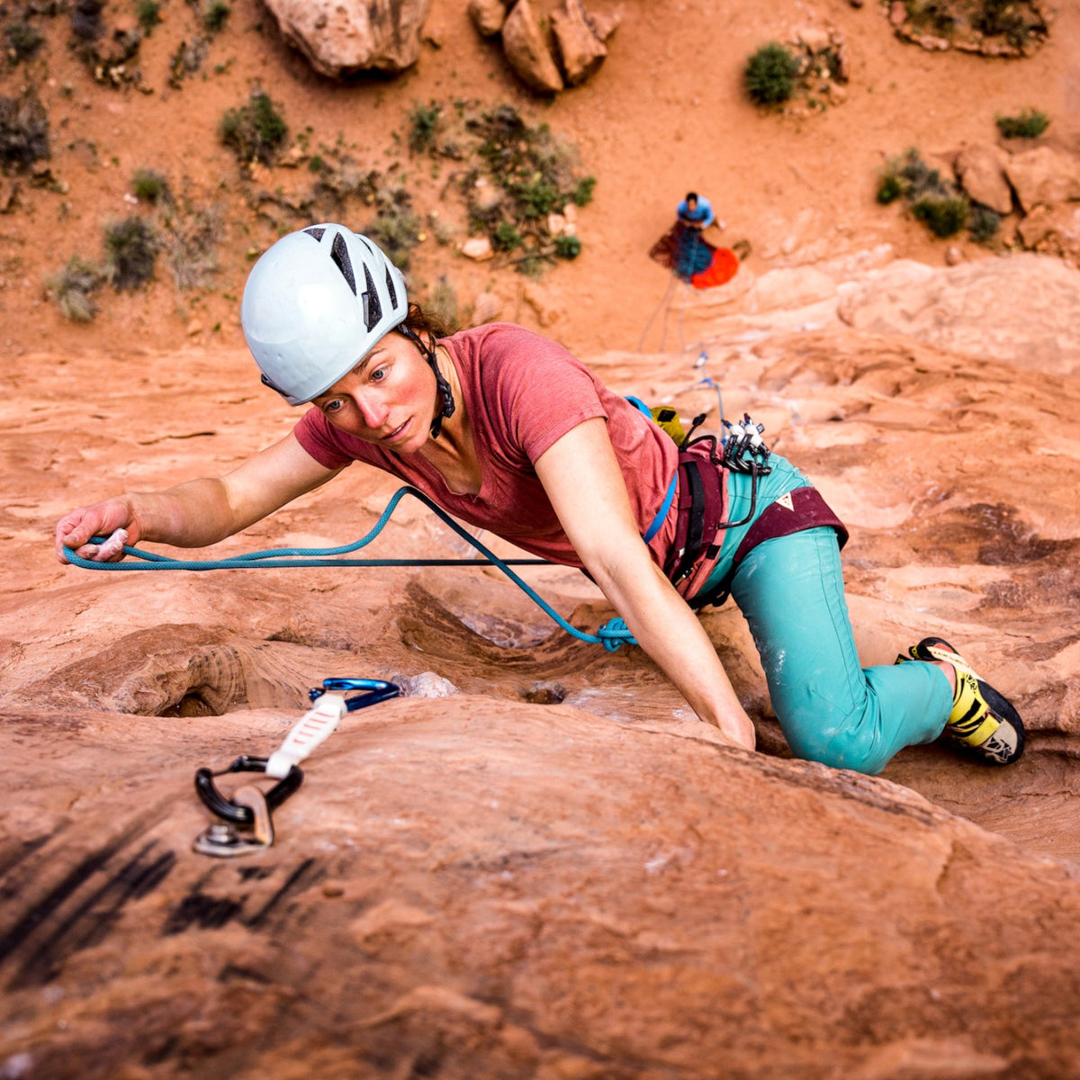 Escaladora con baudrier 4c+ Cuesta Femme en roca roja, usando casco y equipo técnico para escalada deportiva