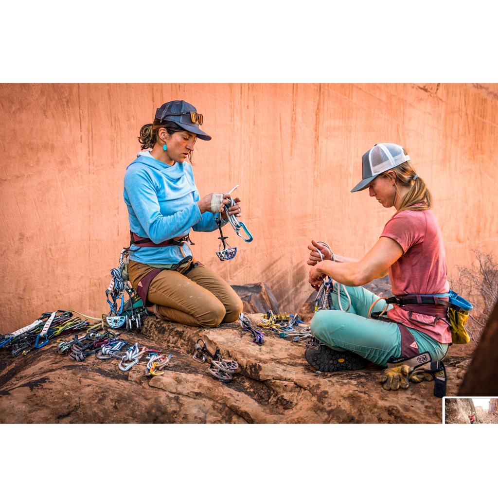 Dos escaladoras con arneses 4c+ Cuesta Femme organizando equipo de escalada en un entorno rocoso al aire libre.